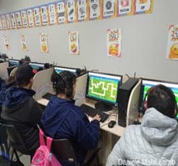 Alunos da EJA em fileira de computadores resolvendo um jogo de labirinto.