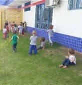 Crianças andam e brincam no gramado, junto à parede branca com azulejos azuis da Instituição.