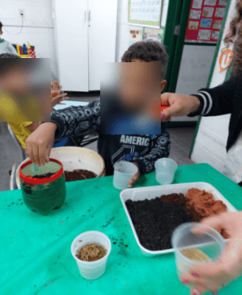 Crianças montando um minhocário em garrafas, com camadas de terra e resíduos.