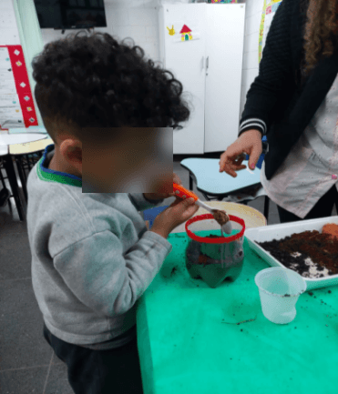 Aluno preenchendo um minhocário com camadas de terra e resíduos orgânicos.