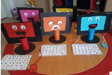 Monitores de computador feitos de papelão, com rostos desenhados, sobre uma mesa.