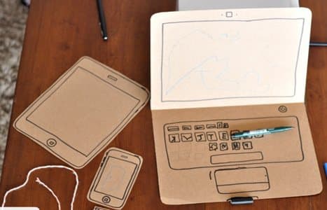 Notebook e tablet construídos em papelão sobre uma mesa de madeira.
