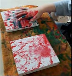 Mão de criança suja de tinta vermelha sobre telas brancas pintadas com marcas vermelhas e verdes.