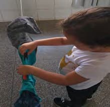 Menino prende com um prendedor uma peça de roupa num varal.