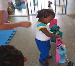 Menina pequena pendura roupas coloridas num varal baixo.