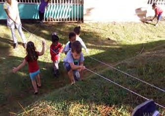 Crianças atravessam um gramado em declive segurando-se em cordas estendidas.