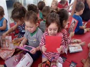 Crianças pequenas sentadas no tatame vermelho seguram e olham livros e cartões ilustrados.