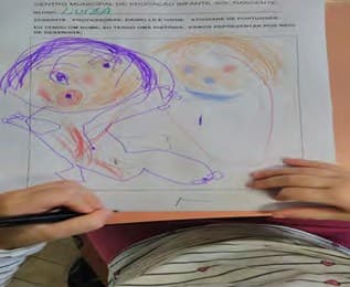 Folha de atividade com o desenho colorido de duas pessoas, feito por uma criança, sobre a mesa.