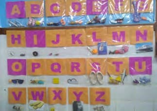 Alfabeto na parede da sala, com cada letra em cartão e, embaixo, um saquinho com objetos que começam com ela.