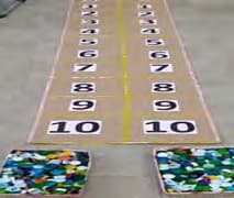 Duas trilhas de casas numeradas de 1 a 10 desenhadas no chão, cada uma terminando num monte de tampinhas coloridas.