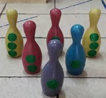Seis pinos de boliche coloridos, cada um com uma quantidade diferente de bolinhas verdes pintadas.