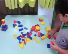 Um menino organiza blocos lógicos de várias cores e formas sobre uma mesa.
