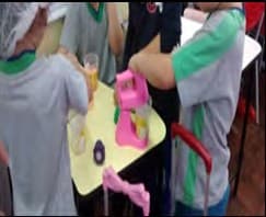 Crianças de touca preparam uma receita em volta de uma mesa com um copo medidor e uma batedeira de brinquedo.