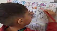 Um menino, de perfil, marca um dia num calendário do mês desenhado em papel.