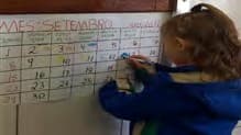 Uma criança de casaco escreve no calendário de setembro preso à parede.