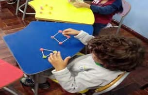 Um menino monta triângulos e quadrados com palitos e bolinhas de massa de modelar sobre a mesa.