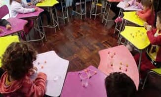 Crianças em mesas coloridas montam figuras geométricas com palitos e bolinhas de massa de modelar.