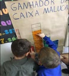 Dois meninos, de costas, pintam as colunas de um gráfico num cartaz intitulado «Ganhador da caixa maluca».