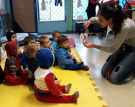 Professora mostra uma imagem a crianças pequenas sentadas no tapete