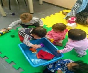 Crianças manipulando objetos em uma caixa, explorando suas propriedades.