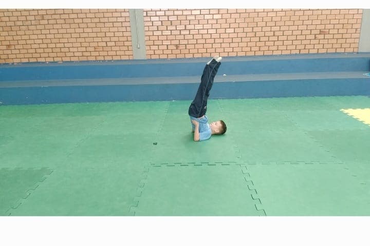 Aluno realizando a vela (ombros apoiados, pernas para cima) sobre o tatame.