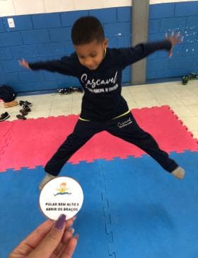 Criança saltando com os braços abertos durante atividade de expressão corporal.