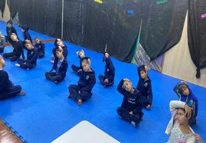 Crianças sentadas em roda realizando uma sequência de movimentos rítmicos.